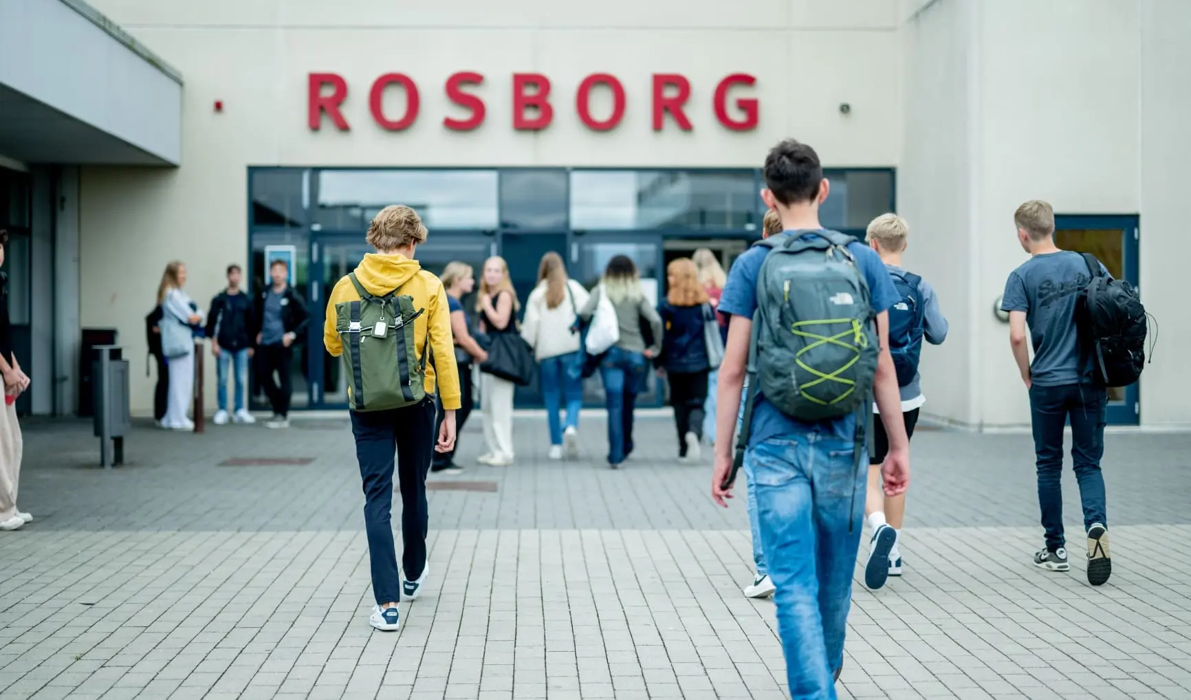 Elever med rygsække går mod indgangen til Rosborg Gymnasium.